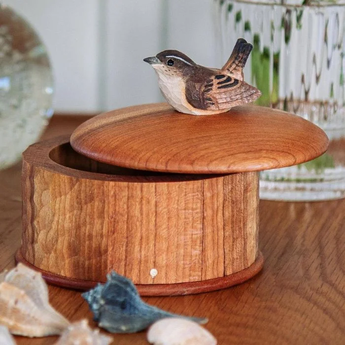 Aufbewahrungsdose Zaunkönig von Wildlife Garden aus Holz mit leicht geöffnetem Runddeckel und geschnitztem Vogel, auf einem Tisch mit Muscheln.